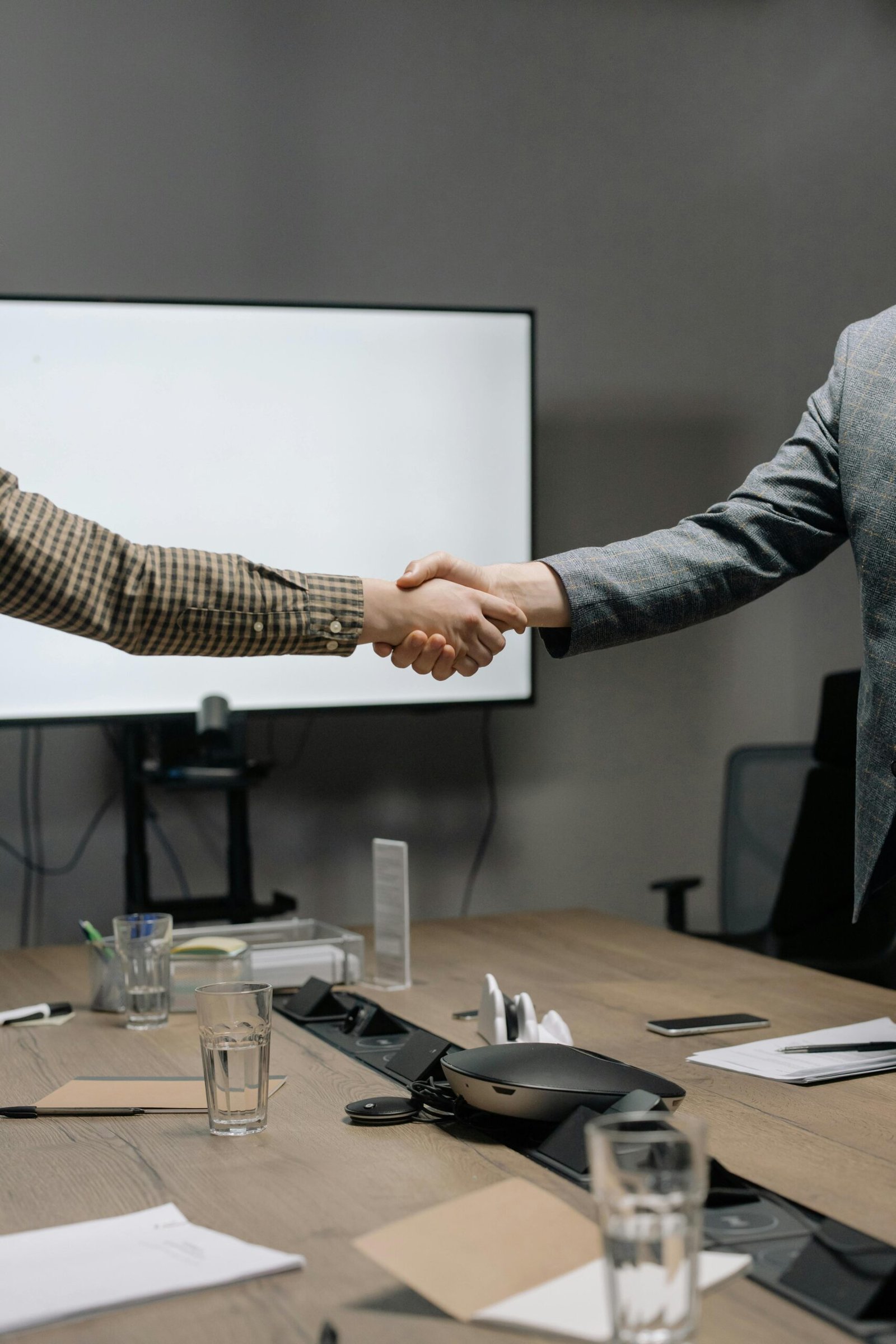 Two business professionals shaking hands in a modern meeting room, symbolizing successful collaboration.