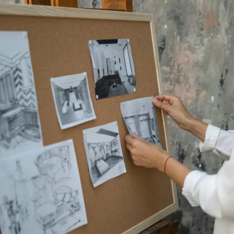 An interior designer setting up sketches on a corkboard in a studio setting.